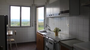 Une cuisine avec une grande fenêtre, un évier, des placards et une chaise.