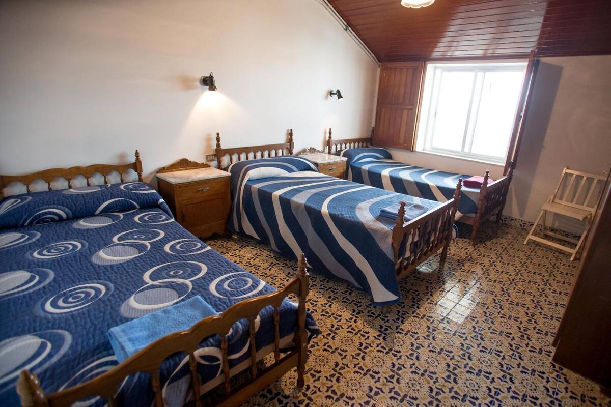 A bedroom with three beds, a wooden ceiling, and a window.