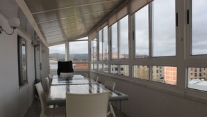 Une salle de conférence dotée d’une grande table et de chaises, de larges fenêtres offrant une vue sur des bâtiments et des collines, et d’un plafond agrémenté d’un luminaire.