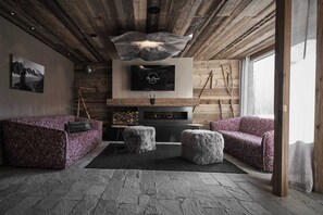 A cozy living room with a fireplace, wooden ceiling, and a TV mounted above it. - Bergsteiger Chalet - The Peak Sölden (Sölden)