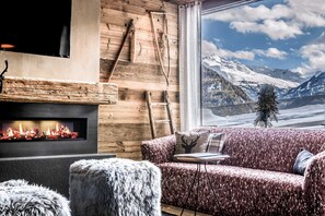 Una habitación acogedora con chimenea, un sofá y vistas a montañas nevadas.