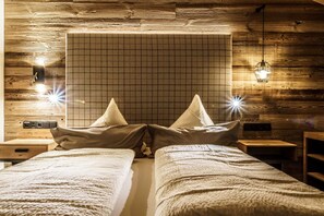 A room with a wooden wall, a grid-patterned headboard, two beds with pillows, bedside tables, and a hanging light fixture. - Bergsteiger Chalet - The Peak Sölden (Sölden)