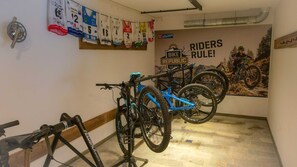 A hallway with two bicycles mounted on a wall, a gear mechanism, and a poster with 'Riders Rule!' text. - Bergsteiger Chalet - The Peak Sölden (Sölden)