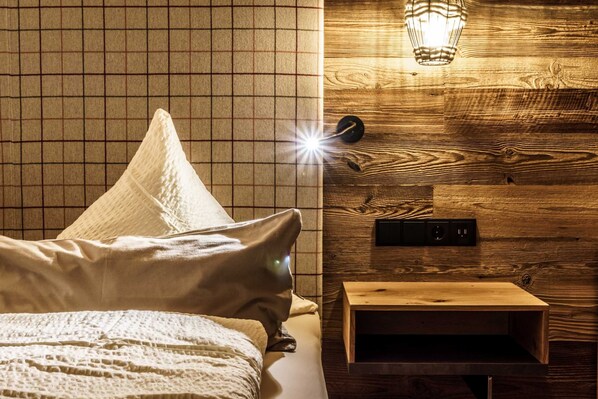 Une pièce comprenant un lit, des oreillers, un mur en bois, un luminaire suspendu et une petite table en bois.