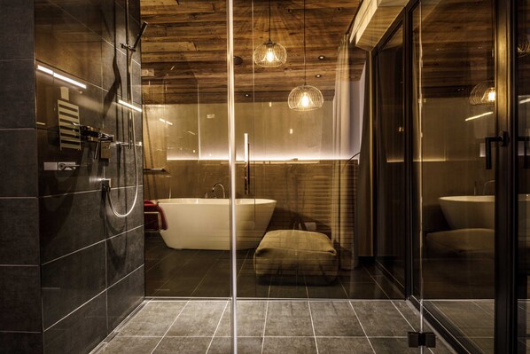 A modern bathroom with a glass-enclosed shower, a freestanding bathtub, and a glass door leading to another room.