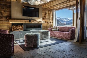 A log cabin interior with a fireplace, television, and a sofa facing a mountain view. - Bergsteiger Chalet - The Peak Sölden (Sölden)