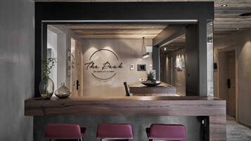 A reception area with a wooden counter, three pink bar stools, and a wall with a circular logo and text.