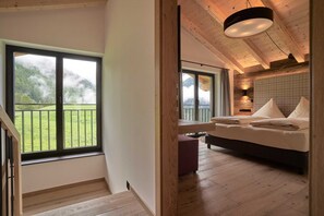 A bedroom with a large window, a bed, a bedside table, and a view of a green landscape.