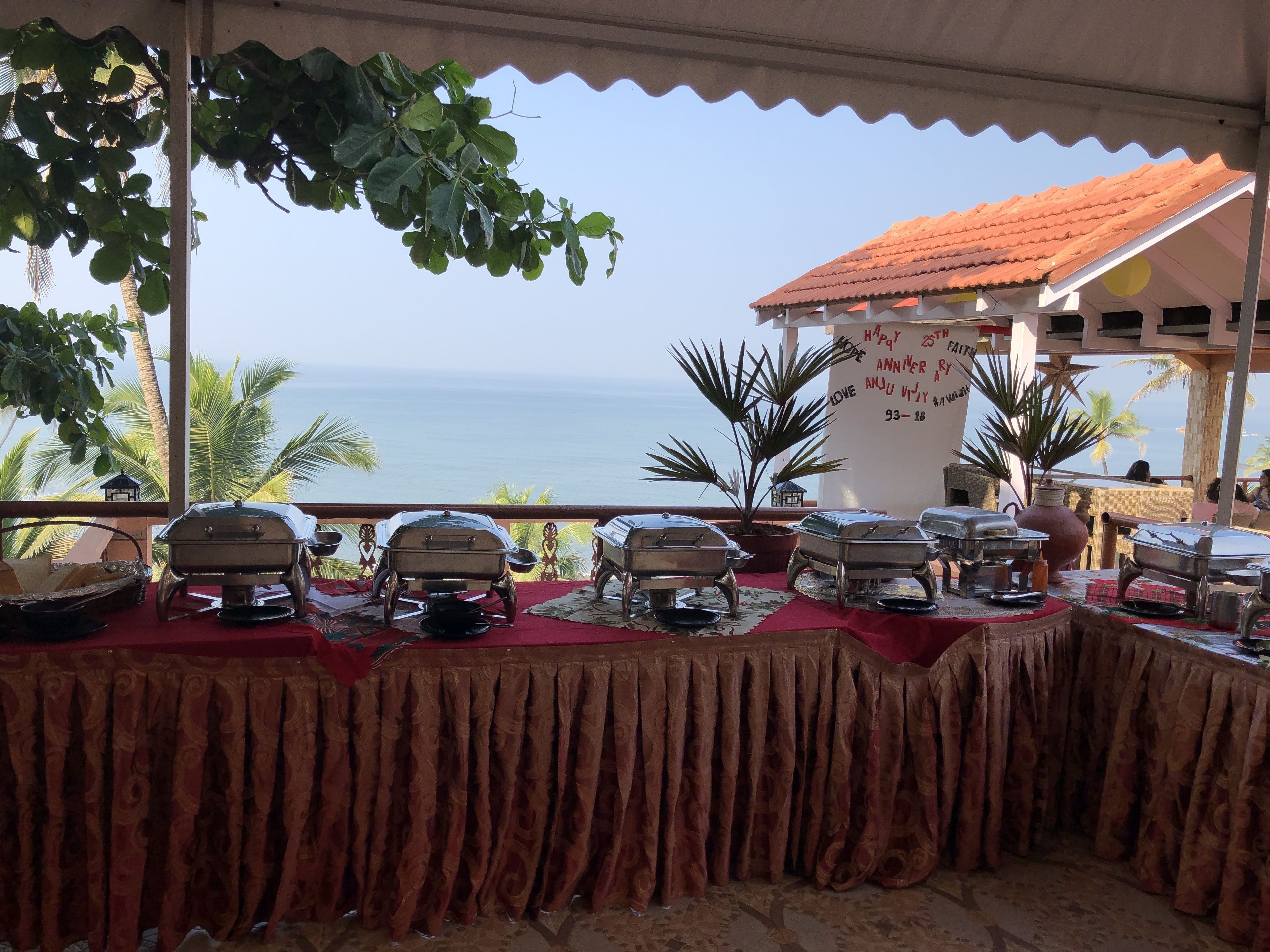 Area pranzo all'aperto coperta con vista sul mare, caratterizzata da un buffet con diverse postazioni di servizio e una parete decorativa con appunti scritti a mano.