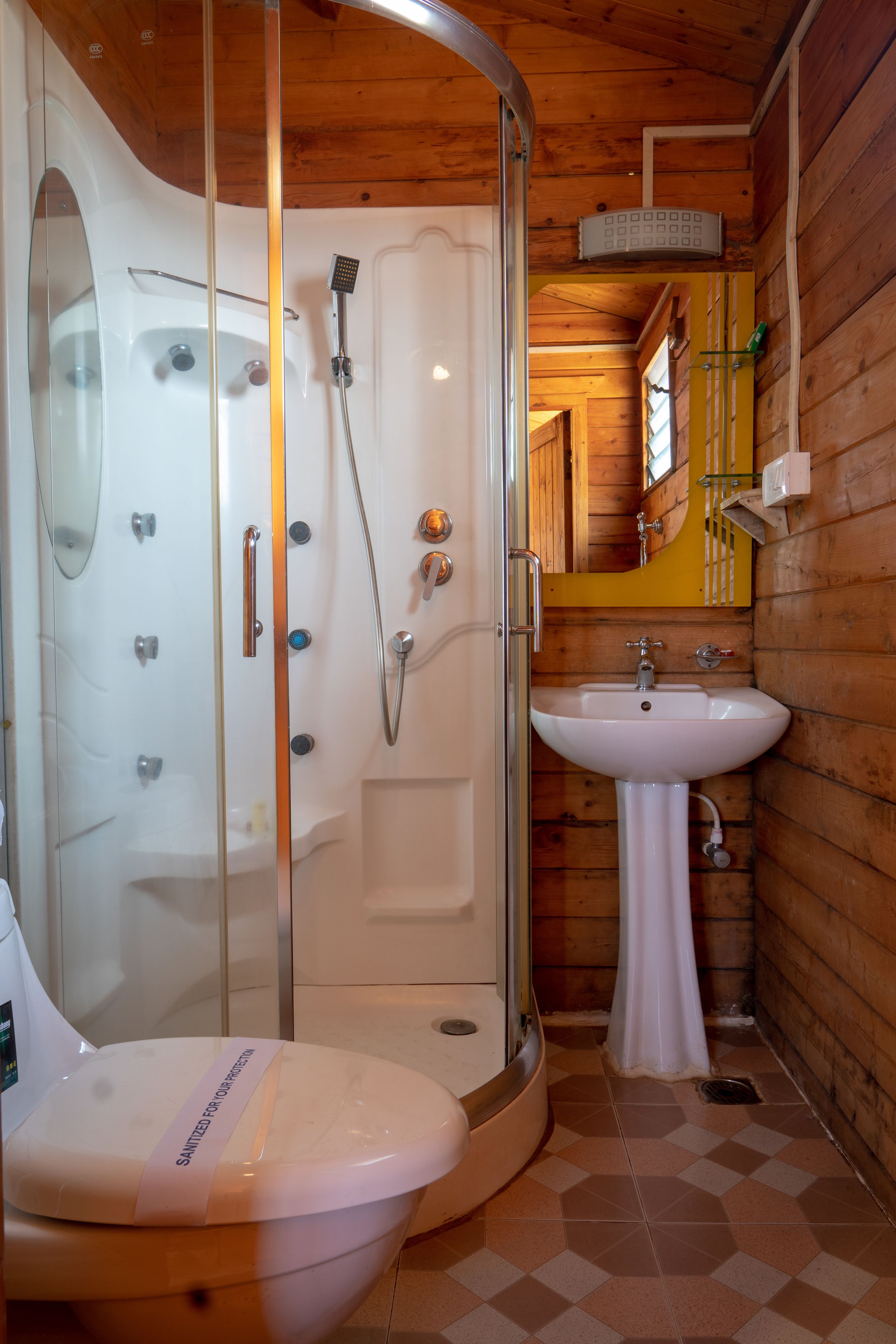 A bathroom with a glass-enclosed shower, a white sink, and a toilet with a sanitization label.