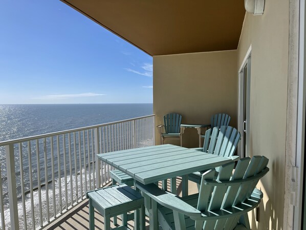 A balcony with a table and chairs, overlooking a beach and the ocean.