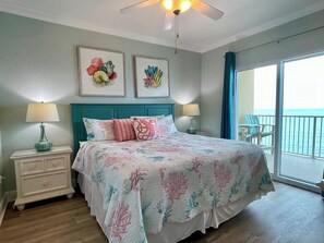 Quarto com cama, duas mesas de cabeceira, ventoinha no teto e vista para o mar através de uma porta de varanda.