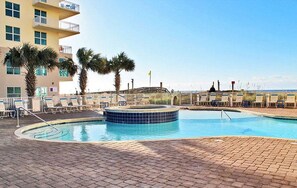 A swimming pool with a hot tub, palm trees, and a building with balconies.