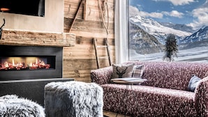 Une pièce chaleureuse avec une cheminée, un canapé et une vue sur des montagnes enneigées.