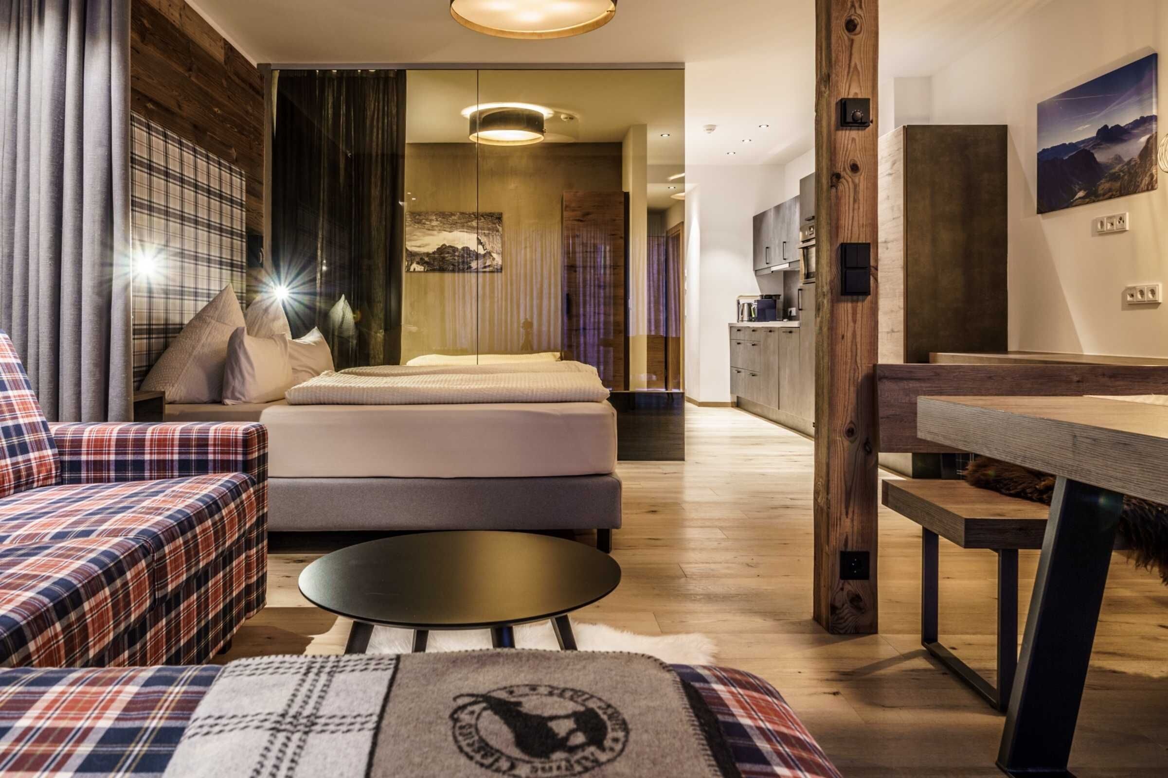 A modern hotel room with a sofa, bed, round table, and a view of the kitchen and bathroom.