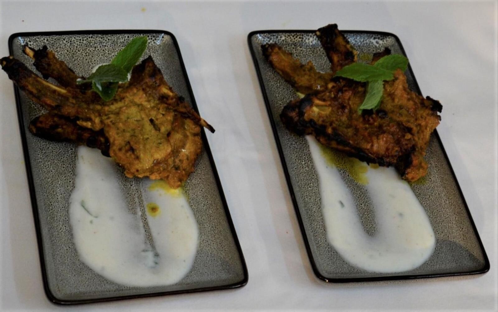 Two square plates with grilled meat and a white sauce, garnished with a green leaf.