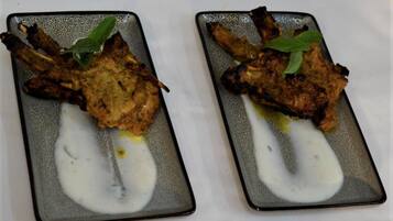 Two square plates with grilled meat and a white sauce, garnished with a green leaf.