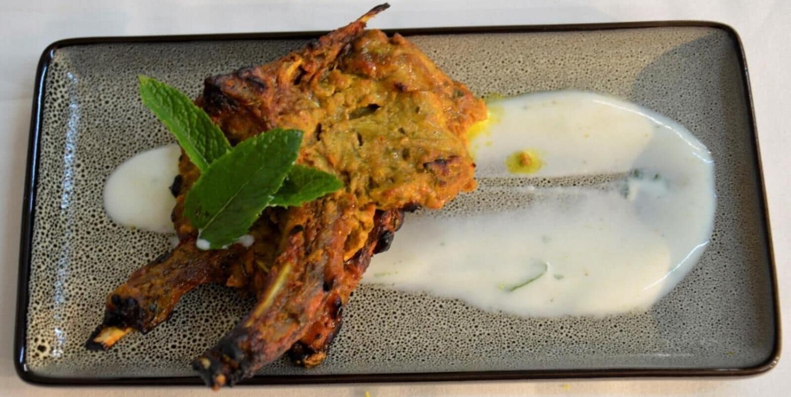 A dish with grilled meat and a creamy sauce on a speckled ceramic plate.