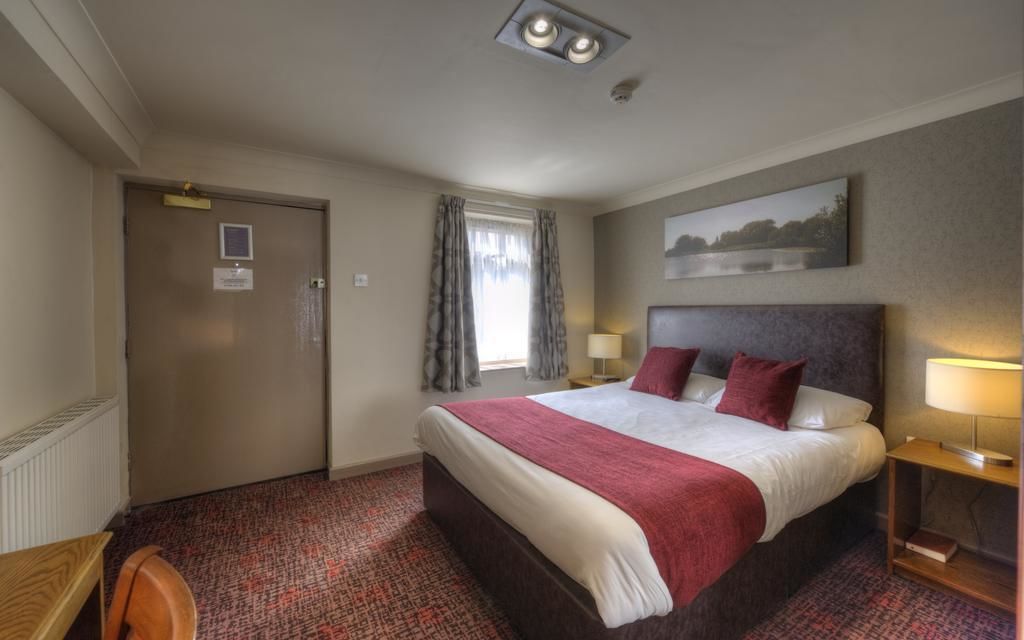 A hotel room with a large bed, a desk, a chair, a window with curtains, a painting on the wall, and a door.