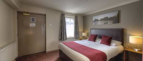 A hotel room with a large bed, a desk, a chair, a window with curtains, a painting on the wall, and a door.