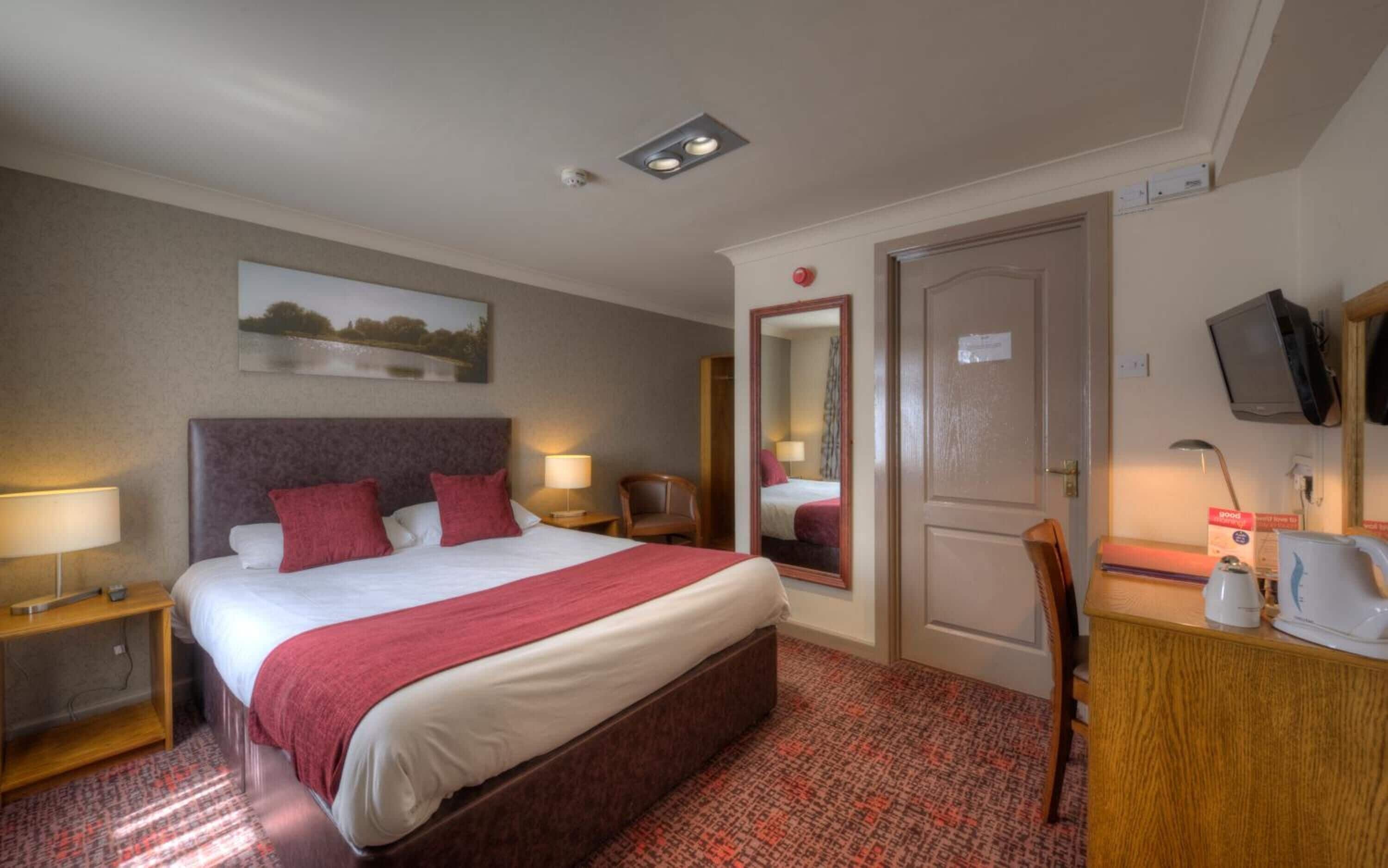 Habitación de hotel con una cama grande, un escritorio con silla, televisión y espejo.
