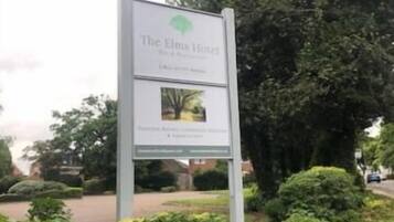 En skylt för hotellet The Elm, med en logotyp och en liten bild av ett träd.