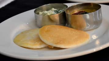 A plate with two pancakes and two small metal cups containing condiments.