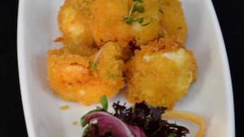 Ein rechteckiger weißer Teller mit frittierten Speisen, einer kleinen Schale grüner Soße und einem Beilagensalat.