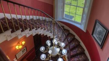 A grand staircase with a chandelier, a view of the outdoors through a window, and a framed picture on the wall.