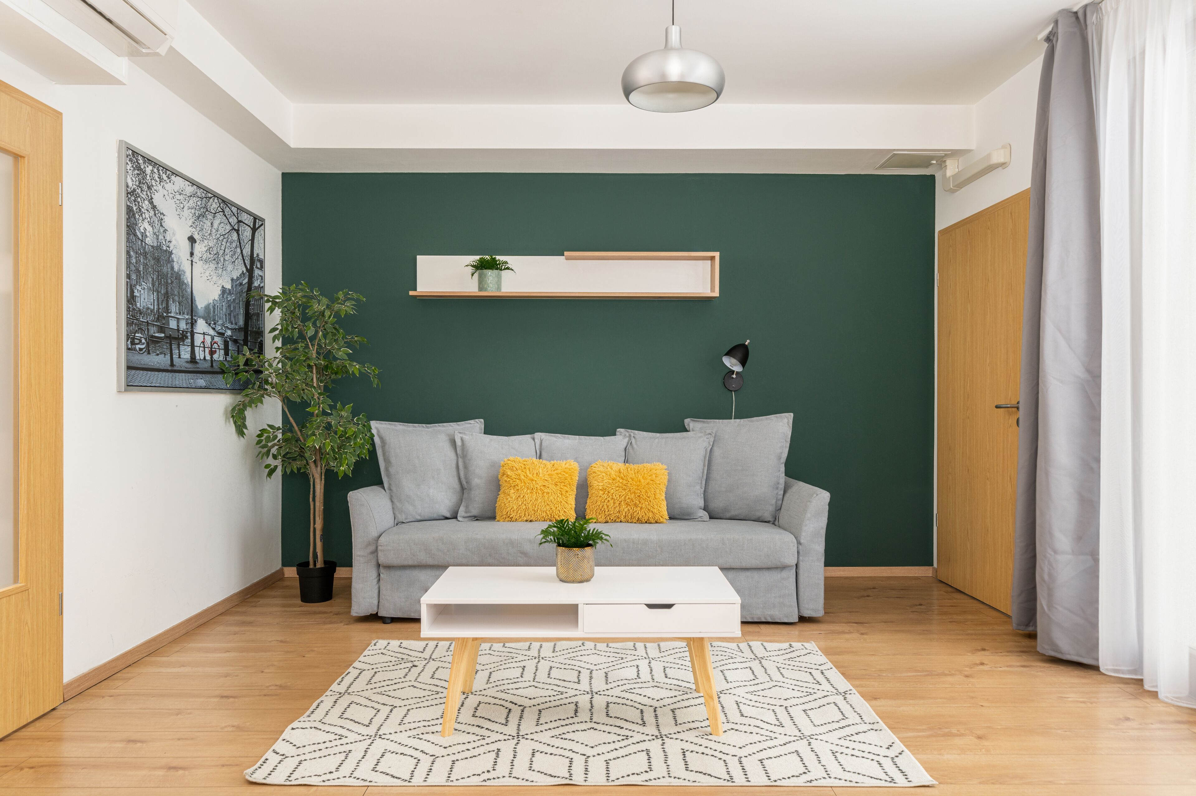A modern living room with a grey sofa, a white coffee table, and a green accent wall.