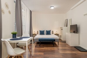 A modern bedroom with a bed, bedside tables, a TV, and a dining area with a table and chairs.