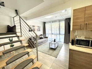 A modern apartment with a staircase, a living area with a sofa, a coffee table, and a kitchen area with a microwave. - Vagabond Downtown (Budapest)