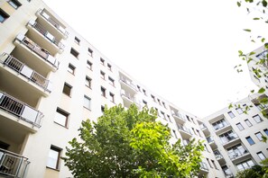 A multi-story residential building with balconies, windows, and a tree in the foreground.
