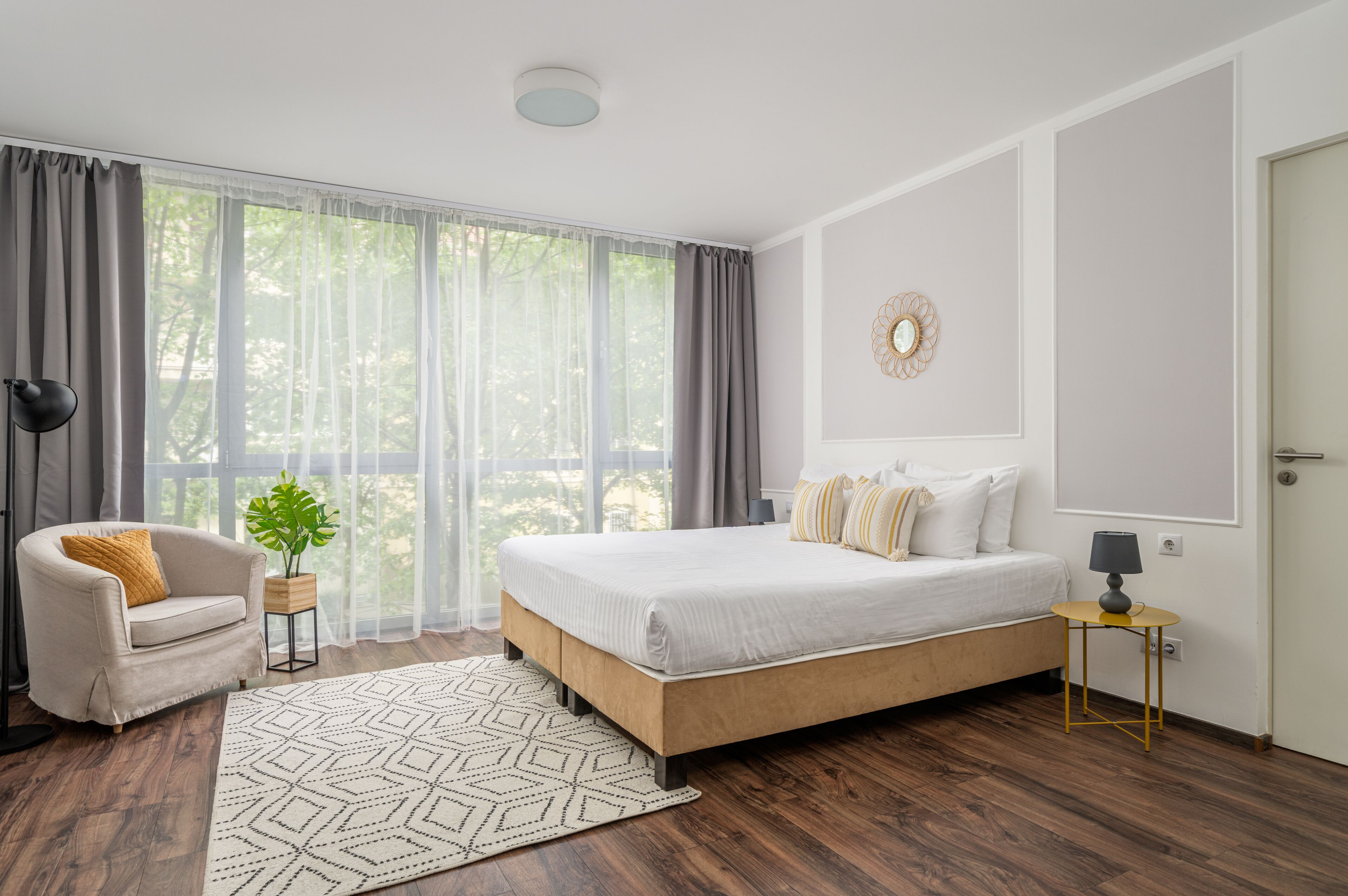Un dormitorio moderno con una cama grande, una mesita de noche, una lámpara, una silla y una ventana con cortinas.