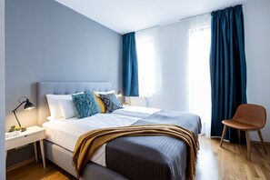 Un dormitorio moderno con una cama grande, mesitas de noche, una silla y un ventanal con cortinas.