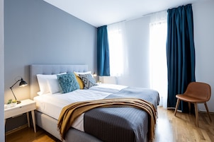 A modern bedroom with a large bed, bedside tables, a chair, and a window with curtains.