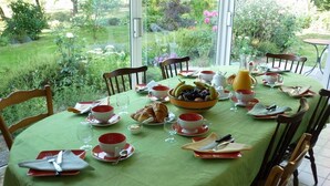 A dining table set for breakfast with a green tablecloth, red and white dishes, and a bowl of fruit. - Chambres d'Hôtes La Semondière (Saint-Thomas-de-Courceriers)