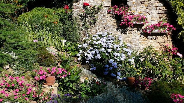 A stone building with a sloped roof, surrounded by a variety of flowering plants and shrubs. - Chambres d'Hôtes La Semondière (Saint-Thomas-de-Courceriers)
