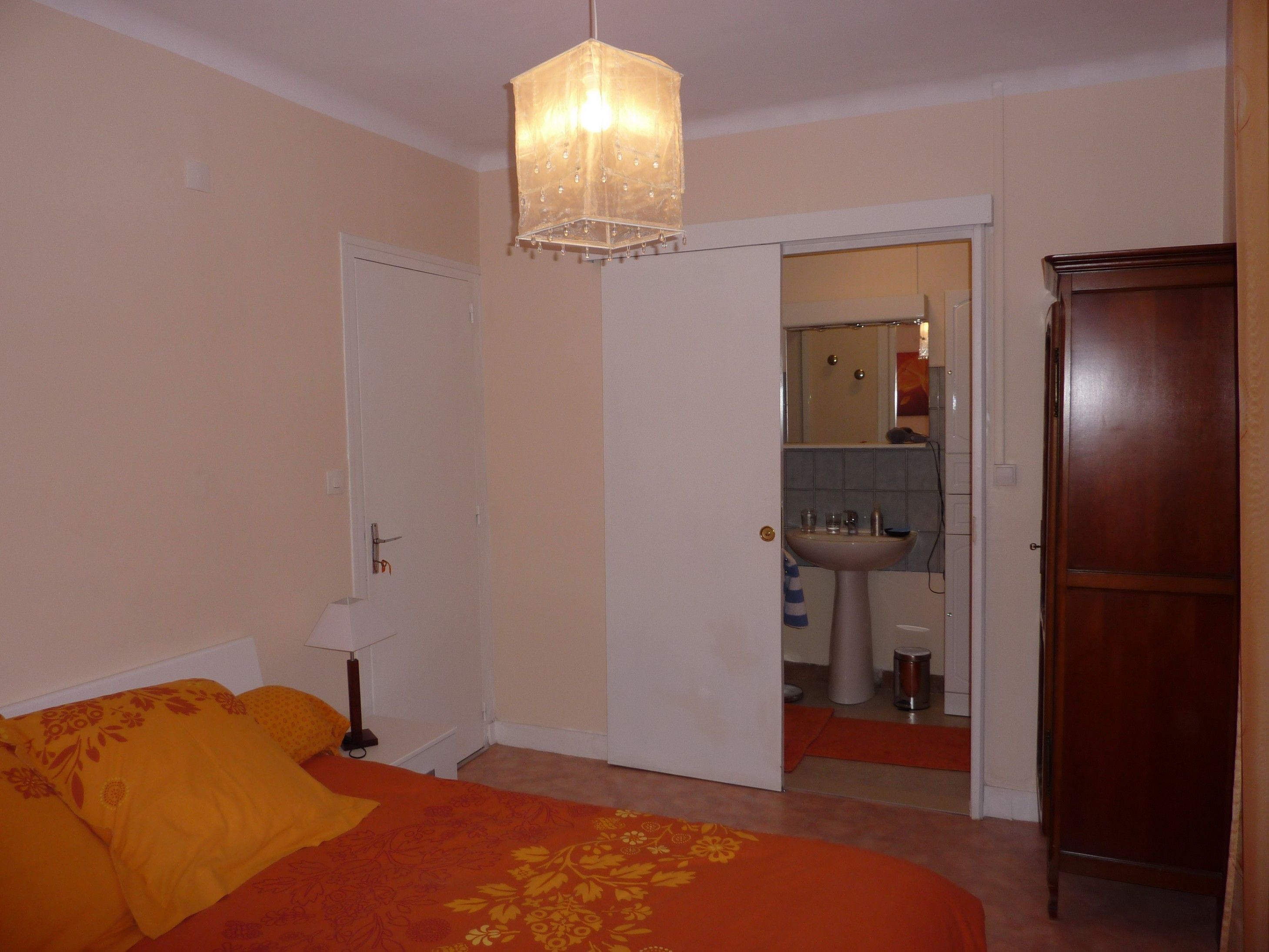 Un dormitorio con cama, mesita de noche, lámpara colgante y puerta que da a un baño.