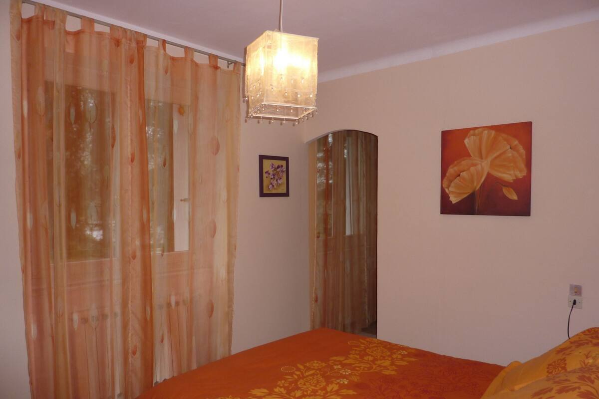 A bedroom with a bed, a hanging light fixture, a door with curtains, and a framed picture on the wall.