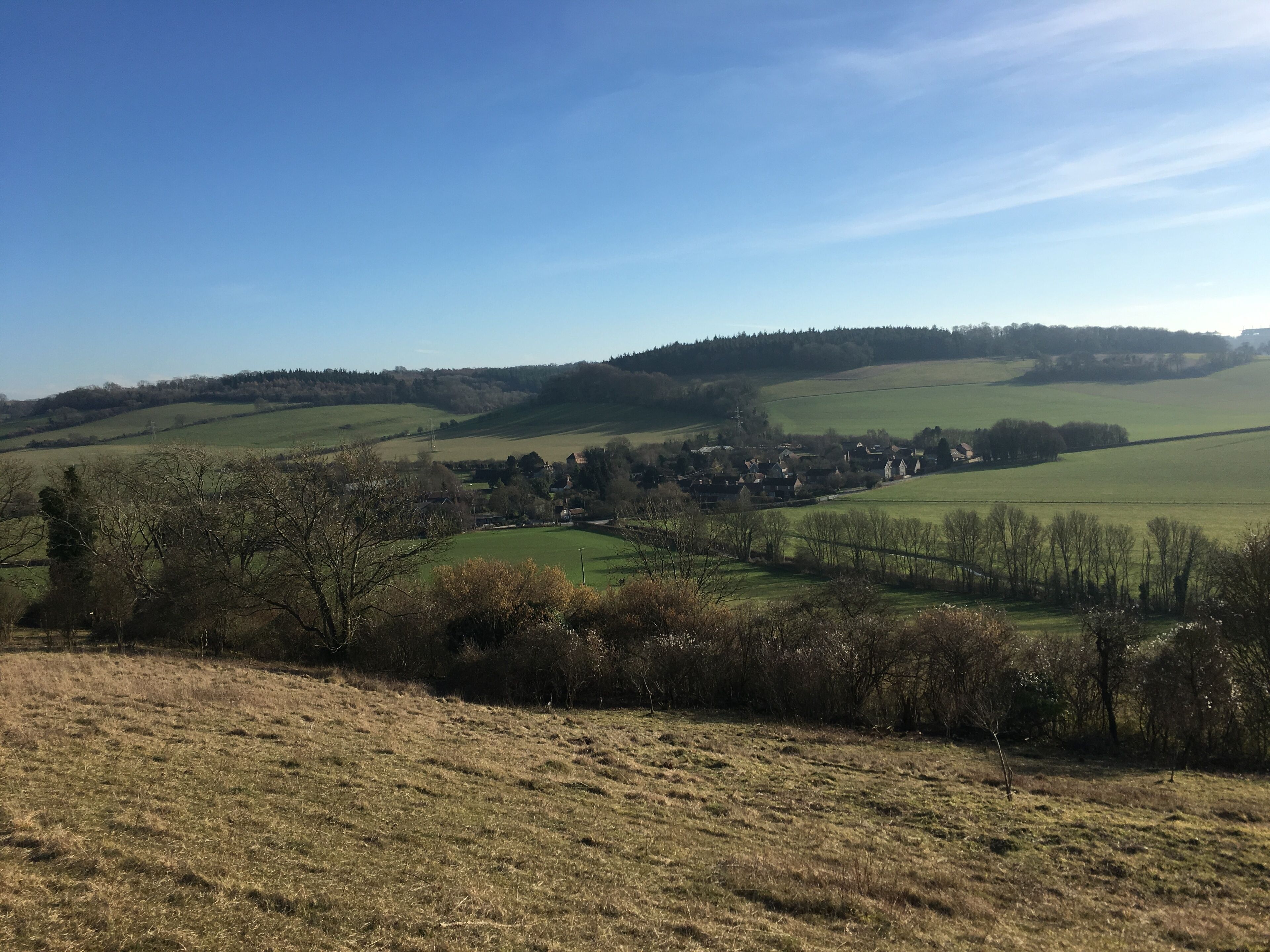 Un paysage rural caractérisé par des collines douces, un petit village et un ciel bleu dégagé.