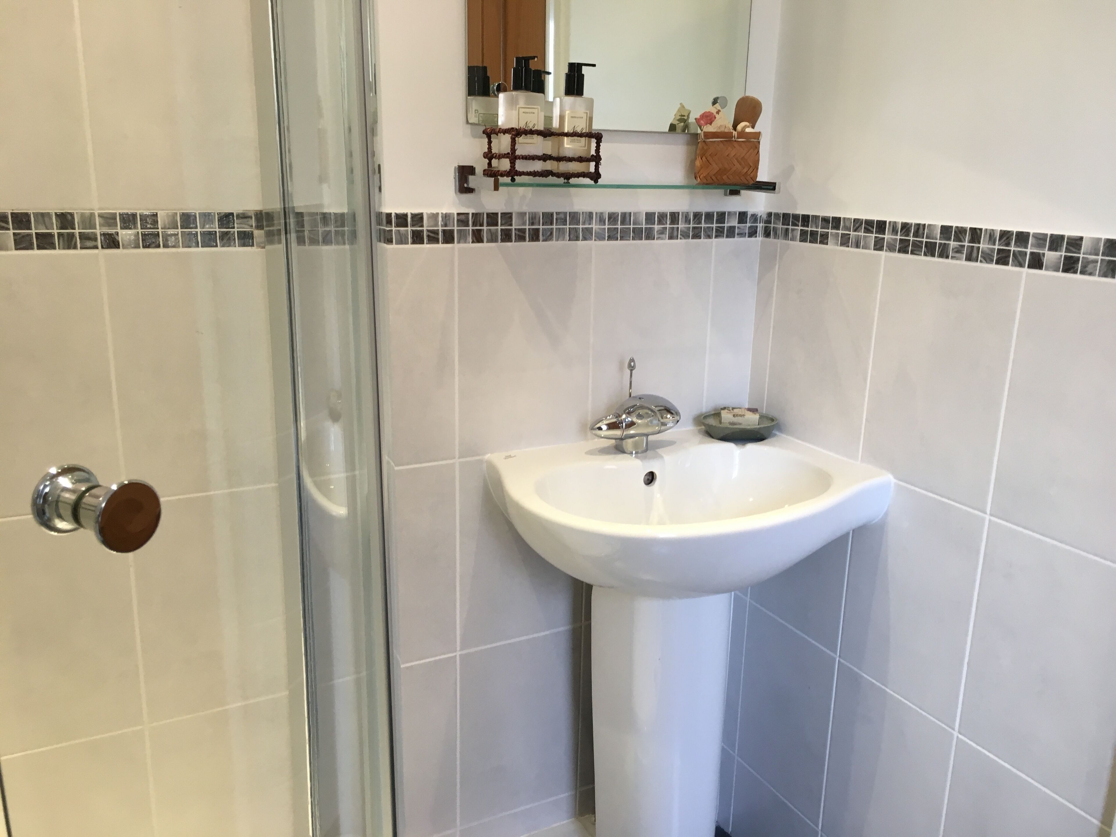A bathroom with a glass shower door, a white sink with a soap dish, and a mirror above the sink.