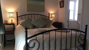 A neatly made bed with a black metal frame, two bedside tables with lamps, a painting on the wall, and a window with a view. - 5 Charlton Mill Way B&B (Chichester)