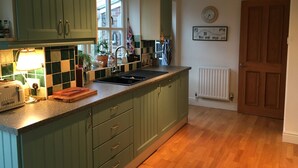 A kitchen with green cabinets, a black sink, and a window with a view of buildings outside. - 5 Charlton Mill Way B&B (Chichester)