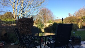 An outdoor patio with a table and chairs, surrounded by a garden and a brick wall. - 5 Charlton Mill Way B&B (Chichester)