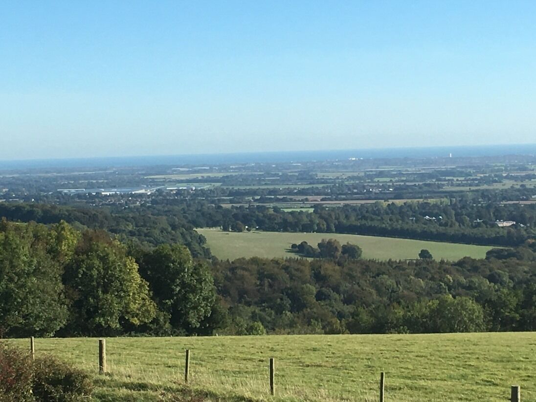 Vista panorámica de un paisaje rural con cielo despejado, que muestra campos abiertos, árboles y edificios lejanos.