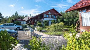 A two-story wooden cabin with a sloped roof, a visible satellite dish, and a paved driveway leading to a parked car. - Guest house Oreskovic (Plitvicka Jezera)