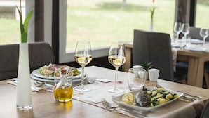 A dining table set with plates, glasses, and a bottle of oil, with a view of greenery outside. - Guest house Oreskovic (Plitvicka Jezera)