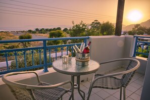 A balcony with two wicker chairs, a small round table, and a metal bucket containing a bottle and glasses. - Villa Amor (Rhodes)