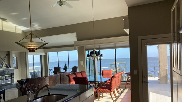 A spacious kitchen with a large island, a dining area with red chairs, and a view of the ocean. - The Bay House Kemah - Houston area Bayfront Home w/ Elevator & Bay Views (Kemah)